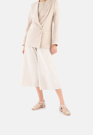 Beige double-breasted blazer, matching wide-leg culottes, and light beige strappy shoes. Smooth fabric, tailored fit, minimalist design.