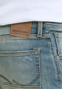 Stražnji džep i pojas svijetloplavih traperica s smešnim kožnim oznakom "JACK & JONES JEANS INTELLIGENCE."