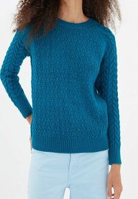 Teal stickad tröja med ett strukturerat mönster, ribbade mudd och nederkant. Långa ärmar med flätstickningsdesign.