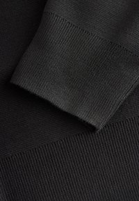 Zwarte gebreide stof met twee secties: één met een geribbelde textuur bij de boord en de andere met een gladdere afwerking.