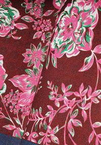 Kwiatowy wzór tkaniny z dużymi różowymi i białymi kwiatami oraz zielonymi akcentami na brązowym, teksturowanym tle.