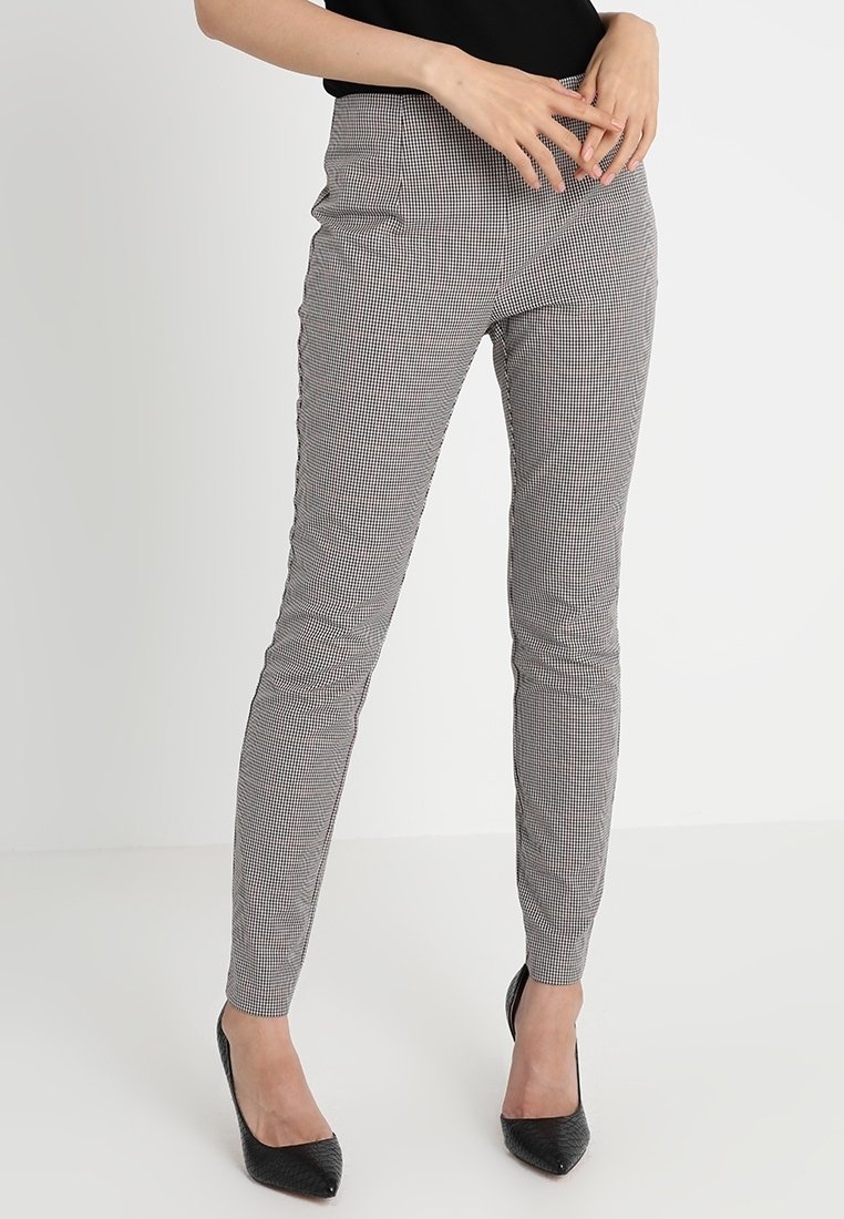 Czarno-białe spodnie w wzór houndstooth o slim fit, średnim stanie i gładkiej fakturze, w zestawieniu z czarnymi, spiczastymi butami.