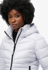 Ljusgrå puffjacka med huva, som har en horisontell quiltad design, framparti med dragkedja och diskret logotyp på dragkedjans dragare.