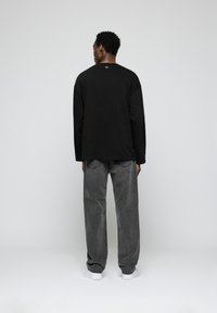 Black long-sleeve shirt and gray loose-fit jeans. The shirt has a plain back, while jeans feature a faded texture with visible seams.