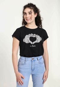 Sort bomulds T-shirt med korte, opfoldede ærmer, prydet med en grå grafik af hænder, der danner et hjerte, og teksten "in love." Matcher med lyseblå jeans.