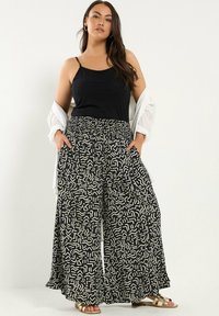 Bredbenta byxor i svart och krämfärgad abstrakt mönster, lättviktsmaterial, elastisk midja, ihopparade med en svart tanktopp och en lätt kofta.