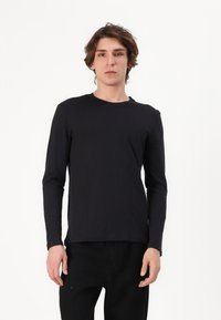 Sort langærmet t-shirt i et blødt, glat stof med rund halsudskæring og afslappet pasform, parret med mørke bukser. Ingen synlige mønstre eller accenter.