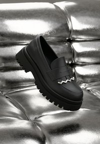 Black leather loafers with a thick textured sole, featuring a decorative silver zigzag accent and smooth finish.