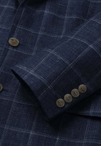 Tmavomodrý károvaný rukáv saka a klopa s štyrmi hnedými gombíkmi na manžete a dvoma gombíkmi vpredu.