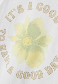 Hvid t-shirt med et stort gult blomstergrafik og teksten "DET ER GODT AT HAVE EN GOD DAG" i beige og sølvfarvet skrift.
