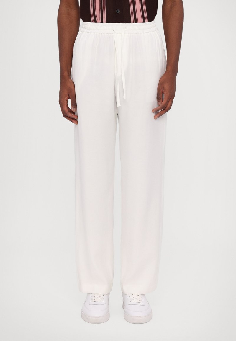 White elastic waist pants with a drawstring, straight cut, soft texture, and seamless design. Worn with white sneakers.