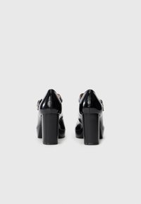 Black leather high-heeled shoes with a glossy finish, rounded toe, and ankle strap. Features a chunky heel and a smooth texture.