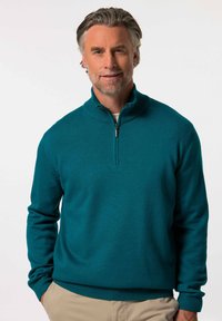 Teal slipover-tröja med hög krage och dragkedja, tillverkad av strukturerat stickat material. Ribbad ärmslut och kant ger detalj.