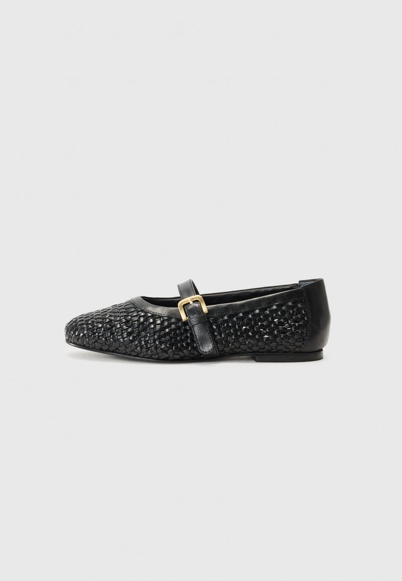 Chaussure plate noire avec une texture tissée, un bout arrondi, des accents en cuir et une petite sangle à boucle sur le coup de pied.