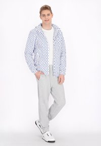 Giacca leggera e con motivo, caratterizzata da disegni blu su sfondo bianco, abbinata a pantaloni di felpa grigi e sneakers bianche con dettagli neri.