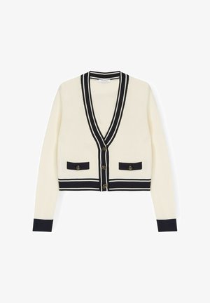 Roomkleurig vest met zwarte biezen en manchetten, V-hals, knoopsluiting en twee voorzakken met knopen.