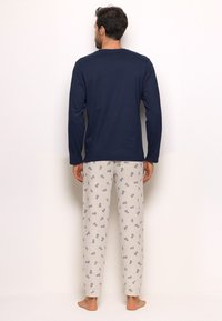Navy long-sleeve shirt paired with light gray pajama pants featuring a repeated blue pattern. Soft fabric, relaxed fit, and cuffed ankles.