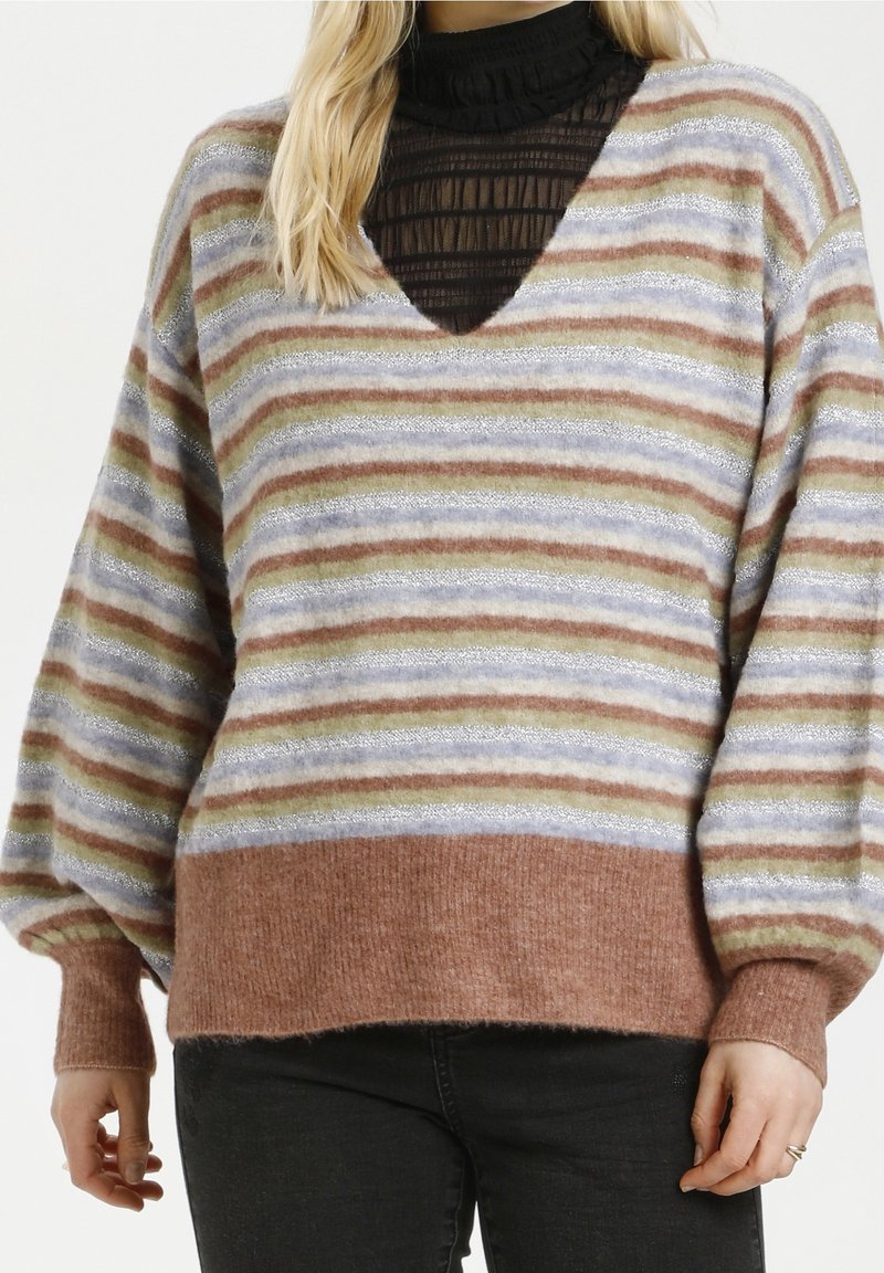 Femme portant un pull en tricot multicolore à rayures avec des manches ballon et des poignets côtelés, sur un haut noir transparent à col haut.