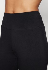 Fekete, magas derekú leggings, puha, rugalmas anyagból. Zökkenőmentes kialakítás és sima textúra jellemzi, finom varrási részletekkel.