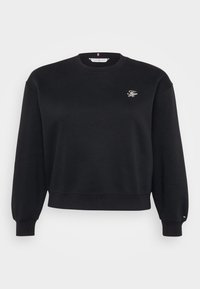 Sweatshirt en polaire noire avec un col rond, des poignets et une ceinture côtelés. Présente un petit logo brodé sur la poitrine. Texture douce.