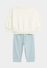 Weißer Baumwollpullover mit langen Ärmeln und elastischem Saum, kombiniert mit hellblau gestreifen Hosen mit zwei Gesäßtaschen.