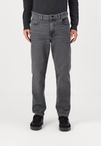 Jeans de mezclilla gris con un corte recto, cinco bolsillos y detalles de costura sutiles. Combinados con zapatillas negras para un look casual.