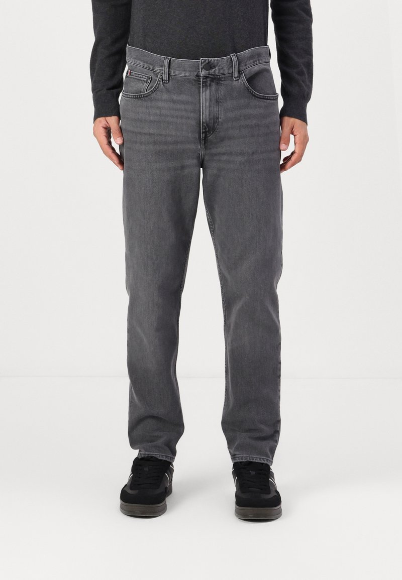 Jeans de mezclilla gris con un corte recto, cinco bolsillos y detalles de costura sutiles. Combinados con zapatillas negras para un look casual.