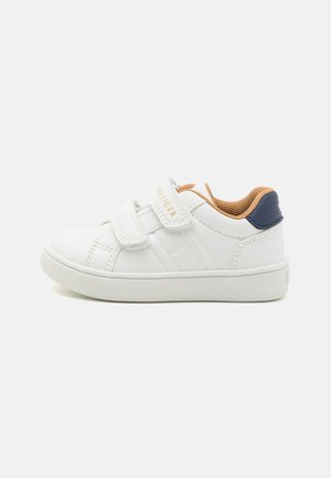 Biały dziecięcy sneaker z podwójnymi paskami na rzep, beżową wyściółką wewnętrzną oraz granatowym akcentem na pięcie, widok z boku na białym tle.