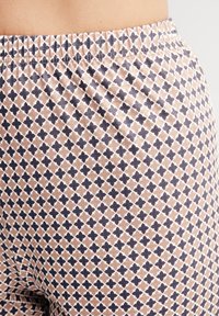 Leggings in hellem Pfirsich mit einem geometrischen Muster aus dunkelblauen Rauten, die weiß umrandet sind. Mit elastischem Bund. Glatte Textur.