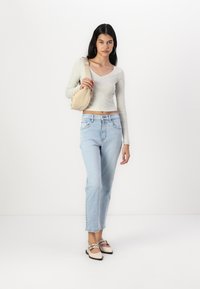 Haut à manches longues gris clair, jeans droits bleu clair, sac à main beige et ballerines bicolores avec des lanières. Design propre et minimaliste.