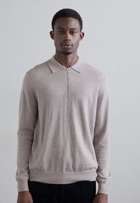Helles beige Strickpullover mit langen Ärmeln, einem Polokragen und einem halben Reißverschluss vorne. Bietet eine weiche Textur und eine figurbetonte Silhouette.