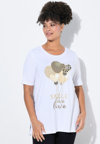 Camiseta blanca de manga corta con gráficos de globos metálicos en dorado, beige y patrones de leopardo, con el texto "SONRÍE AMOR VIVE" debajo.