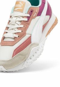 Sneaker PUMA con un design bianco, rosa e viola. Presenta materiali in suede e texture, chiusura con lacci e una suola in gomma chiazzata.