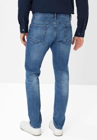 Jeans in denim blu con una vestibilità slim, caratterizzati da vita media, cuciture delle tasche posteriori e leggero sbiadimento, abbinati a sneakers bianche.