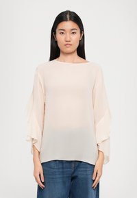 Ljusbeige, genomskinlig blus med volangformade, klockärmar. Löst fit, rund halsringning, matchad med blå denim. Slät textur, delikat tyg.