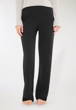 Pantaloni neri elasticizzati con vita elasticizzata, texture liscia e design svasato, visti dalla vita fino alle caviglie, indossati a piedi nudi.