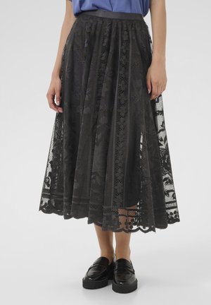 Black lace midi skirt with pleats, floral patterns, and a scalloped hem. Paired with a fitted top and chunky black loafers.