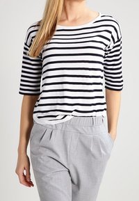 T-shirt in cotone a righe bianche e blu navy, con scollo rotondo ampio e maniche a tre quarti, abbinata a pantaloni grigi plissettati.