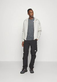 Men's athletic outfit featuring a light gray zip jacket with textured sleeves, a dark gray fitted t-shirt, and black cargo pants with side pockets.