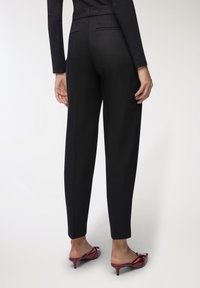Pantaloni neri sartoriali con vita alta, tasche laterali e tessuto liscio, abbinati a mule con tacco rossi.