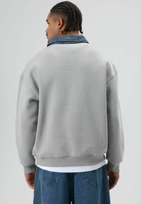 Grijze sweat met een denim kraag, relaxte pasvorm, geribbelde manchetten en zoom. Heeft een gladde textuur met contrasterende kleurdetails.