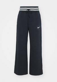 Námořnické modré široké teplákové kalhoty s proužkovaným elastickým pasem, přední kapsou a bílým vyšitým logem Nike na levém stehně.