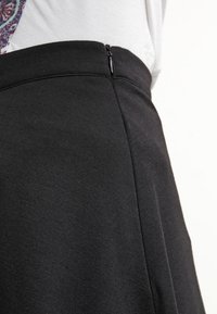 Jupe noire en tissu lisse, avec une fermeture éclair sur le côté. Le design est évasé, avec une silhouette épurée et simple.