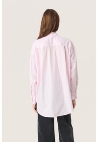 Camicia button-up rosa con maniche lunghe e orlo arrotondato. Tessuto liscio con una leggera lucentezza, dotata di un colletto classico e piega sul retro.