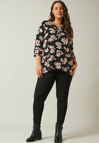 Top nero floreale con maniche a tre quarti, caratterizzato da un collo a V e un motivo floreale bianco e rosso, abbinato a jeans skinny neri e stivali alla caviglia.