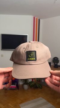 Svetlo rjava bejzbolska kapa z črnim kvadratnim obližem z rumenim logotipom in napisom »FORMER«. Kapa je iz teksturirane tkanine in ima ukrivljen ščitnik.