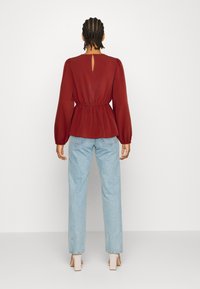 Bordó peplum blůza s nabíranými rukávy, zúženým pasem a detailem klíčové dírky na zádech, doplněná o světlé modré džíny rovného střihu.