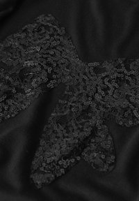 Nahaufnahme eines schwarzen Stoffs mit strukturierter Spitze und kleinen Pailletten, die ein sternförmiges Dekormuster bilden.