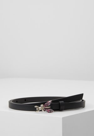 Schwarzer Ledergürtel, auf einer weißen Oberfläche aufgewickelt, mit einer dekorativen silbernen Schnalle in Form einer Biene mit rosa und roten glitzernden Flügeln.