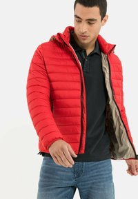 Rote Daunenjacke mit Kapuze, gefüttert mit einem gesteppten Design, mit einem Reißverschluss vorne und kontrastierender beiger Fütterung. Getragen über einem schwarzen Poloshirt.